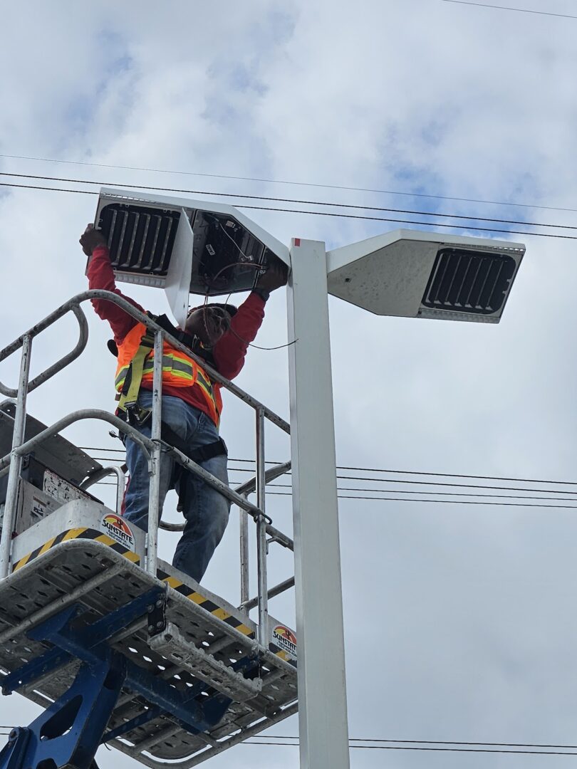 Worker installing solar panels on streetlights using a hydraulic lift.