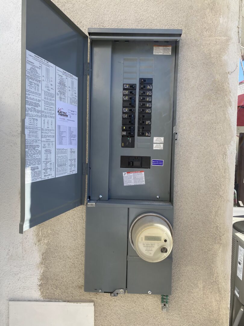 Open electrical panel with circuit breakers and a meter attached on the wall.