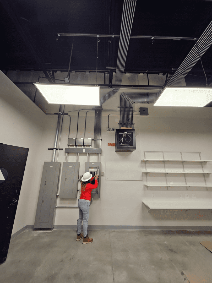 Person in red jacket inspecting electrical panels in a large industrial room.
