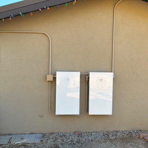 Two white electrical boxes mounted on a beige exterior wall.